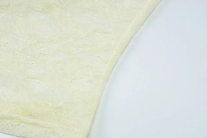 Detailed macro view of pale yellow floral lace fabric with intricate cutout patterns