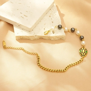 Golden snake bracelet with pearls and dark beads on textured beige fabric background