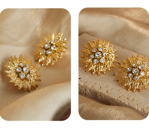 Detailed view of sun-shaped gold earrings with zircon stones on silk and stone background