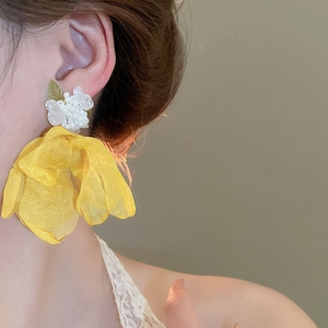Detail view of large yellow tulle flower earrings with white bead clusters and green leaves