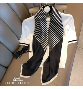 Detail view of a black and white striped silk scarf styled with a white top and accessories