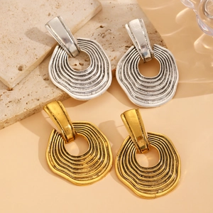 Macro detail of geometric wavy gold and silver earrings on a natural stone background