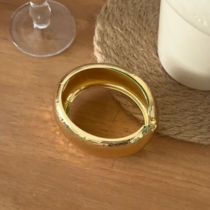 Gros plan d'un large bracelet doré minimaliste avec une surface irrégulière et un éclat métallique
