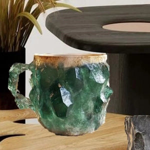 Detalle de taza de café de cristal mineral verde con borde dorado en mesa de madera