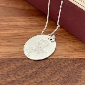 925 silver necklace with vintage rose engraved oval pendant on walnut desk background