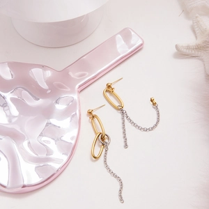 Detailed view of two-tone gold and silver tassel chain earrings on decorative tray