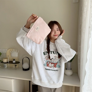 Pink corduroy cosmetic bag with textured fabric held by hand in a cozy home setting