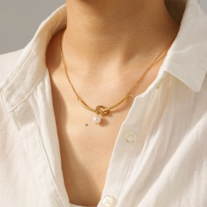 Dettaglio ravvicinato della collana con pendente a nodo e perla in oro 18k