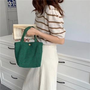Model holding a green and black houndstooth woolen handbag in a cozy home setting.