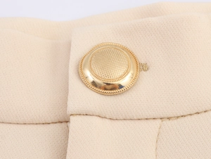 Macro detail of beige suit trousers showing textured gold button and premium fabric weave