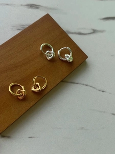 Close-up of heart-shaped pendants on silver and gold hoop earrings on a wooden base
