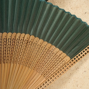 Dark green silk folding fan with bamboo frame featuring intricate hollow carvings
