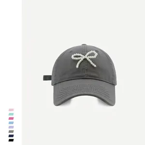 Detail of a dark grey cotton baseball cap featuring a white pearl bow embellishment