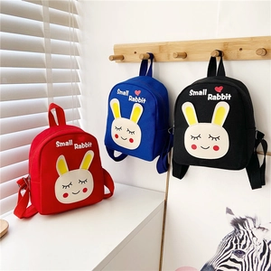 Three children's rabbit backpacks in red, blue, and black colors on wooden hooks