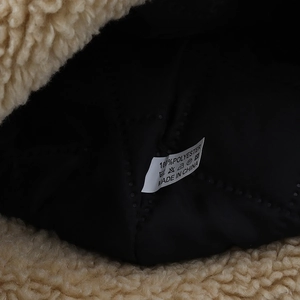 Detail of warm beige sherpa fleece with black quilted lining and 100% polyester care label
