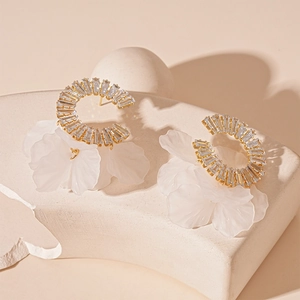 Detail of C-shaped gold earrings with zircon stones and frosted white flower petals