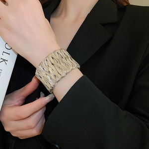 Detailed close-up of a wide golden braided metal bracelet on a model wearing black suit