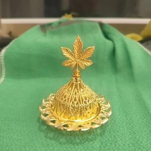 Golden filigree incense burner with hollow weave texture and leaf top on green background