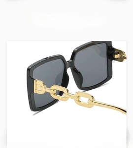 Detail of square sunglasses featuring black frames and a stylish gold chain temple design