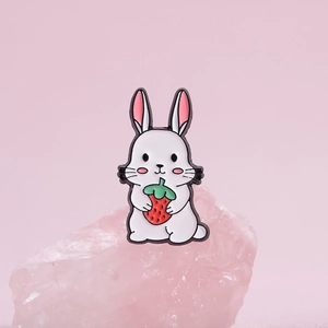 Détail d'une broche en émail représentant un lapin blanc tenant une fraise rouge