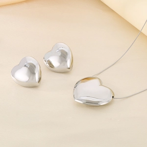 Ensemble collier et boucles d'oreilles cœur argenté poli sur tissu beige doux