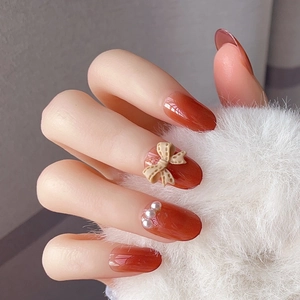 Detail of amber gradient press-on nails with 3D bows, pearls and glossy mirror finish