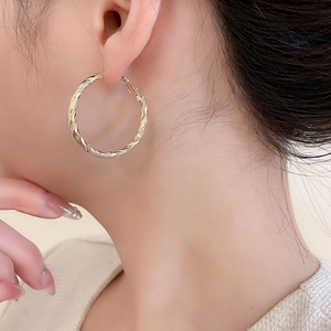 Gros plan d'un modèle portant des boucles d'oreilles créoles torsadées dorées