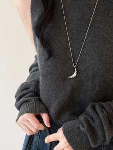 Detail of silver croissant moon pendant on fine chain styled with a dark knit sweater