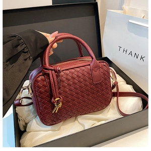 Detail of burgundy hand-woven Boston bag with gold hardware in an elegant gift box