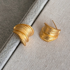 Macro detail of golden C-shaped metal earrings featuring a brushed textured surface finish