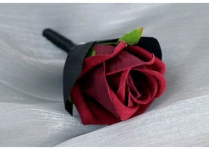 Close-up of deep red velvet rose boutonniere with green leaf for wedding groom