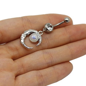 Detailed view of silver moon navel ring with iridescent stone held by hand for size