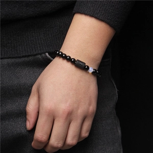 Detail shot of a beaded bracelet with zodiac charm on a model wrist against black backdrop