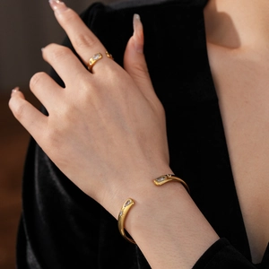 Close-up of golden teardrop zircon open bracelet and ring set on black velvet background