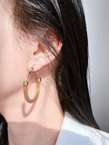 Close-up of a large gold hoop earring with textured metal mesh on a side profile model