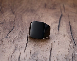 Macro shot of polished black stainless steel square ring on a wooden texture background
