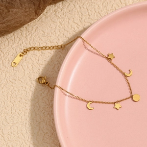 Detail of 18K gold plated chain with star and moon charms on a decorative ceramic plate