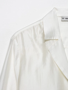 Detail view of white acetate satin shirt neckline with premium stitching and pearlescent texture