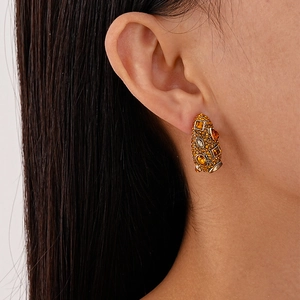 Close-up of geometric gold earrings with amber rhinestones worn by a model