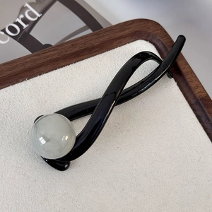 Close-up of black twist hair claw clip with large gray pearl on a wooden tray detail