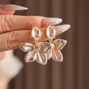 Detail of floral earring with champagne petals, pearls and crystals held by a hand