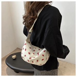 Detail of white corduroy shoulder bag featuring red strawberry embroidery and wide strap