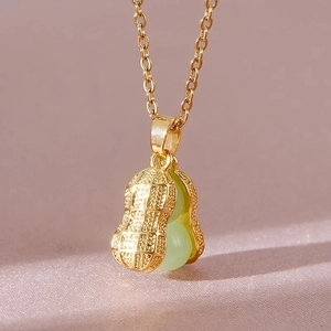 Macro shot of a golden peanut pendant necklace with two green beads on pink silk