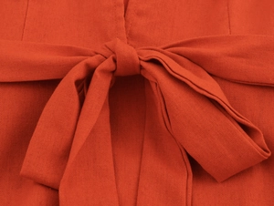 Detail of the orange-red V-neck dress featuring a waist tie bow in breathable linen fabric