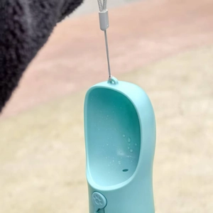 Close-up of portable blue pet water bottle featuring a wide drinking trough and paw button