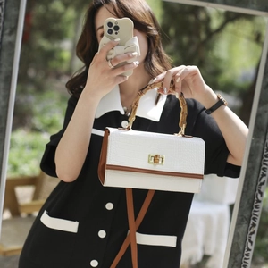 Close-up of a white croc-embossed handbag with a bamboo handle and golden twist-lock closure