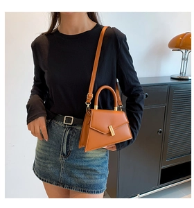 Brown trapezoidal crossbody bag with gold buckle and top handle worn by a model