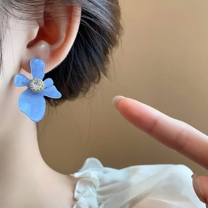 Dettaglio ravvicinato di orecchino a fiore in resina blu con zircone sul lobo