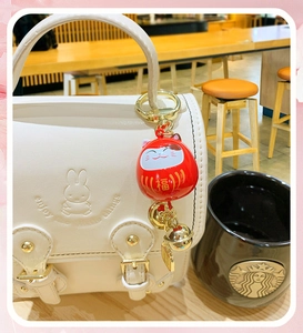 Detail of red Maneki Neko charm with golden bell hanging on a white Miffy handbag