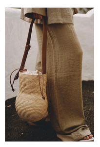 Detail of handwoven straw bucket bag featuring a brown leather strap and linen drawstring